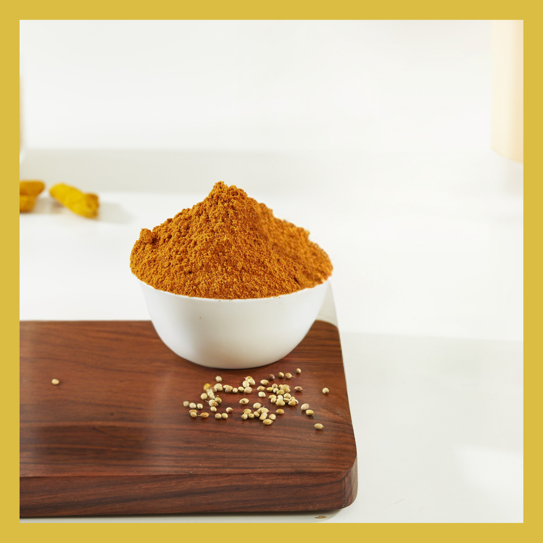 White bowl filled with Authentic Sambar Podi spice powder on wooden board with coriander seeds