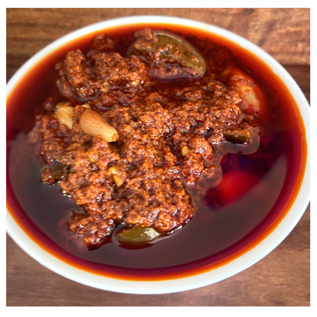 Close-up of Malu's Avakkai pickle with garlic in a white bowl showing rich spicy texture and oil