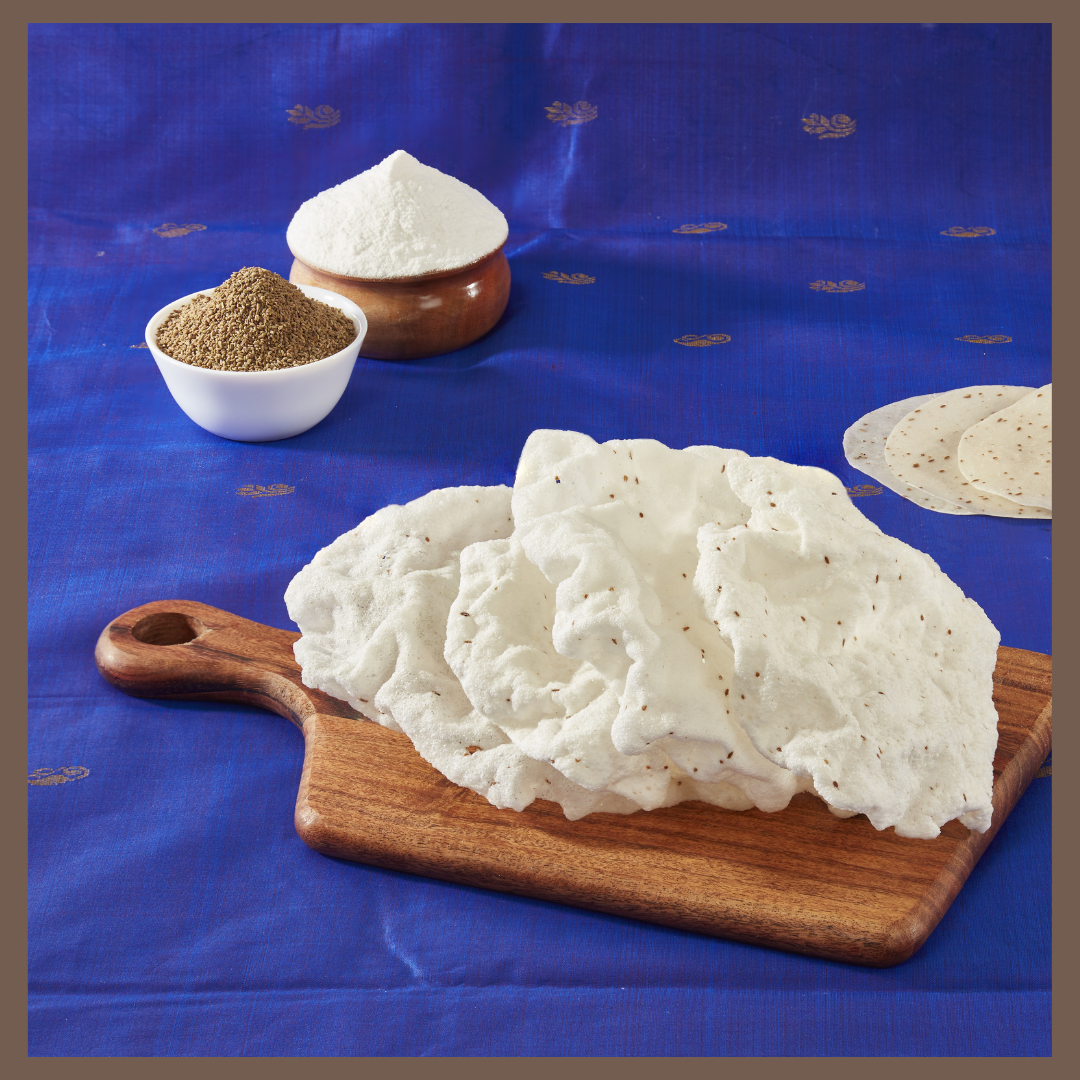 Traditional Indian rice crackers Elai Vadam stacked on wooden board with spices and flour in background