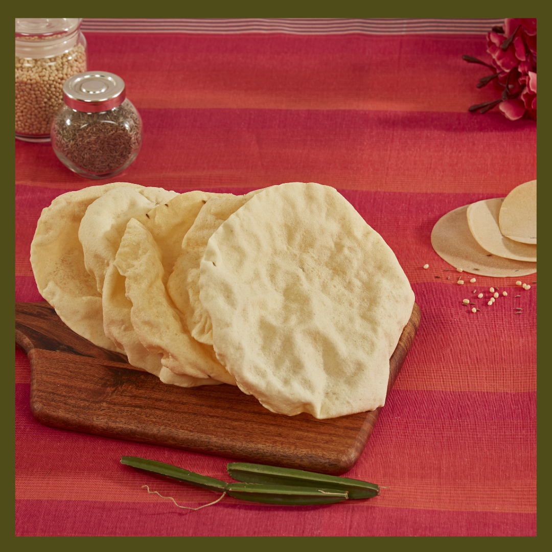 South Indian Appalam snacks displayed on wooden board with spices and green chilies on red cloth