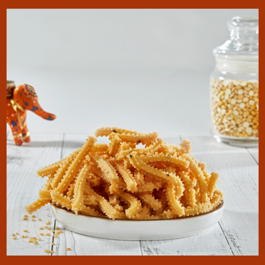 Plate of homemade Indian travel snacks Murukkus on a white wooden table with decorative jar and figure in background