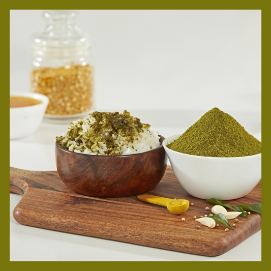 Malu's curry leaves podi with garlic served in white and wooden bowls on a wooden board with garlic cloves and curry leaves