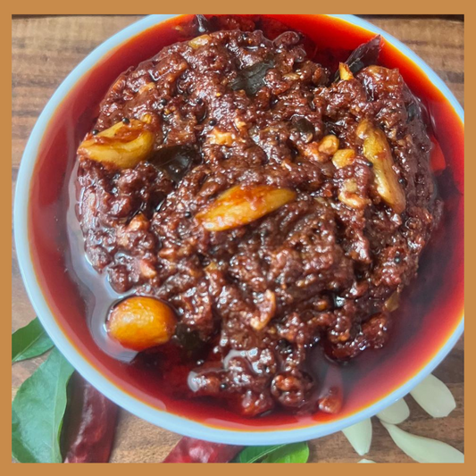 Malu's spicy and flavorful Garlic Thokku online in a white bowl with whole garlic and red chilies