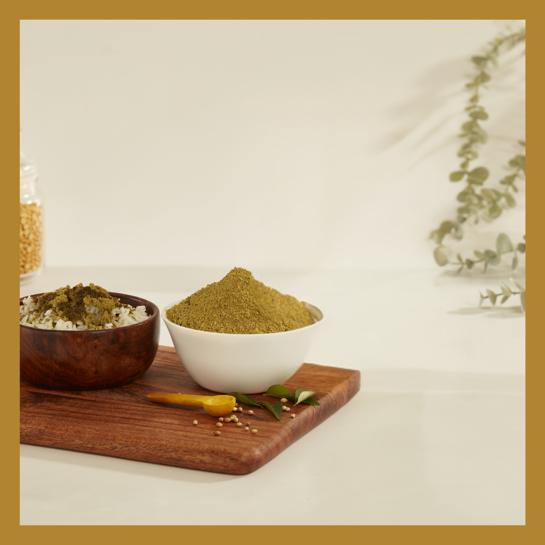 Malu's South Indian curry leaves powder in a white bowl with curry leaves and mustard seeds on a wooden board