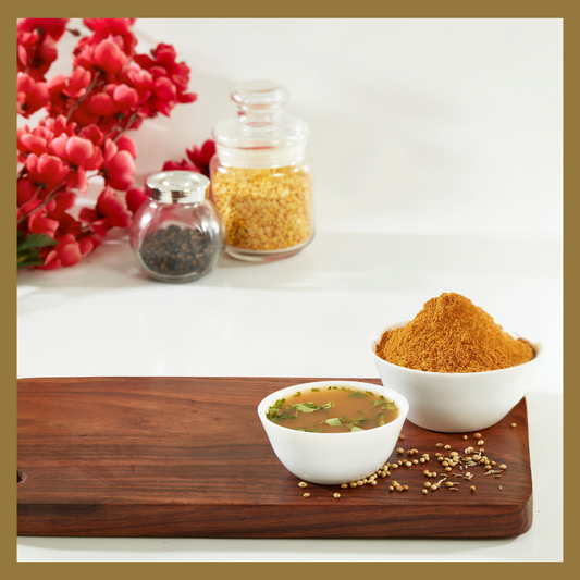 Traditional rasam powder 180g in white bowl with prepared rasam soup on wooden board by Malu's